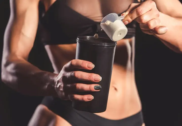 Kobieta dodaje proszek proteinowy do shakera.