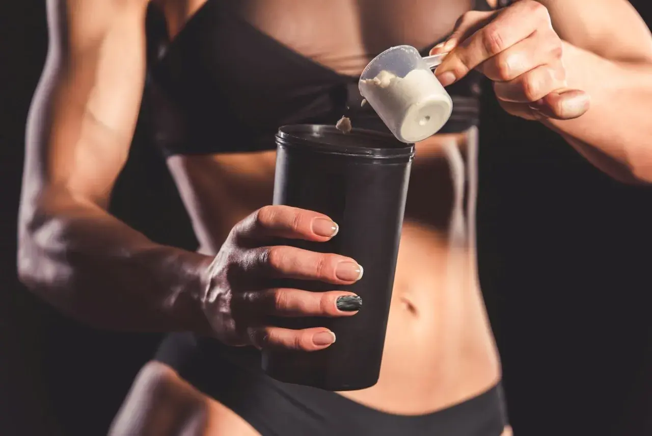 Kobieta dodaje proszek proteinowy do shakera.